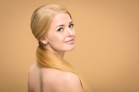 attractive naked blonde girl with long hair smiling at camera isolated on beigeの写真素材