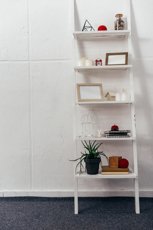 shelves with red clock, wooden frameworks, plant, books, bottle with seashells and candles on white backgroundの写真素材