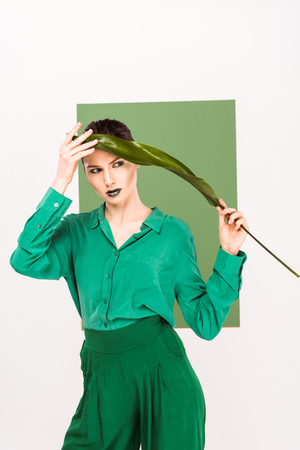 beautiful stylish woman holding leaf, looking away and posing with sea green on backgroundの写真素材