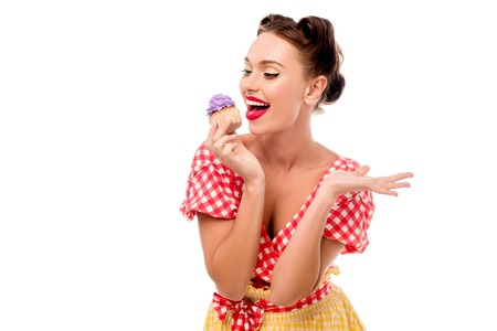 Pretty pin up girl tasting cupcake with purple cream isolated on whiteの写真素材