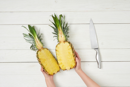 cropped view of female hands holding pineapple halves near knife の写真素材