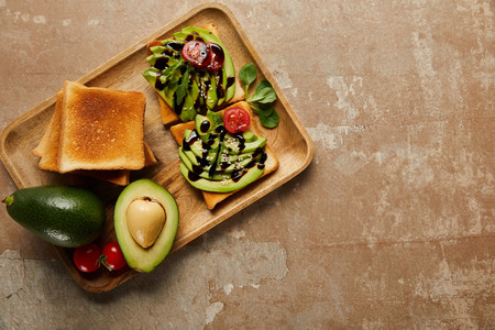 top view of toasts with avocados, cherry tomatoes on wooden chopping board,  brown backgroundの写真素材