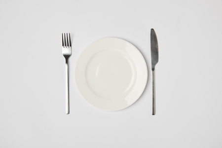 top view of porcelain plate with fork and knive on grey backgroundの写真素材