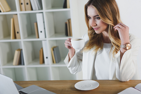 cheerful woman holding cup with drink in officeの写真素材