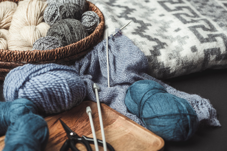 close up view of knitting, scissors and knitting needles on dark tabletop with blanketの写真素材