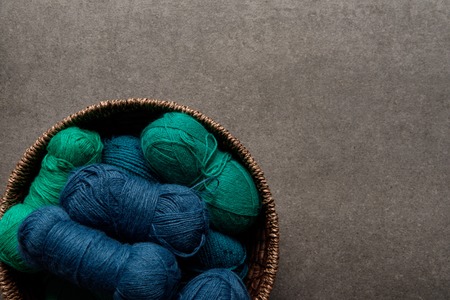 top view of green and blue yarn clews in wicker basket on grey background