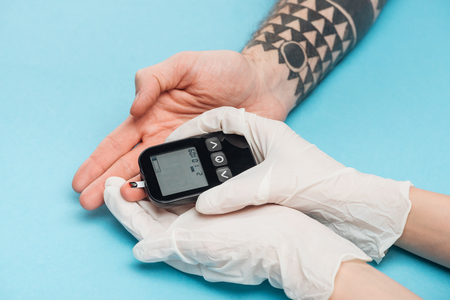 cropped view of woman in gloves with glucometer on blue backgroundの写真素材