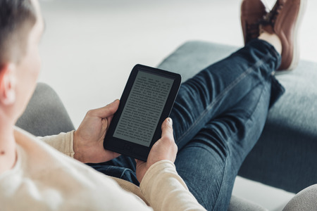 cropped view of man reading e-book while sitting in armchair at home