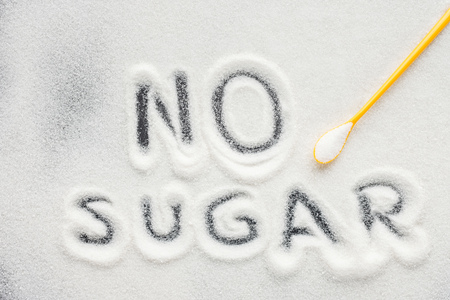 top view of "no sugar" lettering written on granulated sugar with plastic spoonの写真素材