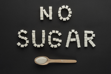 flat lay of "no sugar" lettering made of cubes with wooden spoon isolated on blackの写真素材