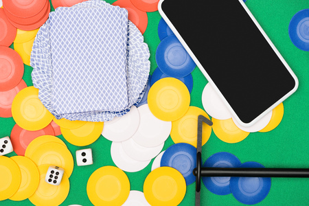 top view of green poker table with multicolored chips, playing cards,  dices, stick and smartphone