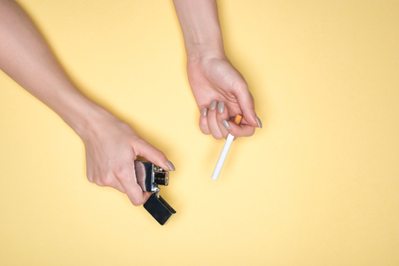 Partial view of woman holding cigarette and cigarette lighter isolated on yellowの写真素材