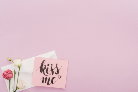 top view of flowers, envelope and card with 'kiss me' lettering isolated on pinkの写真素材
