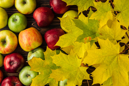 top view of ripe multicolored apples and yellow maple leaves on wooden tableの写真素材