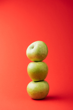 stack of three ripe green apples on red backgroundの写真素材