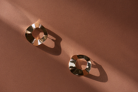 top view of beautiful luxury golden earrings on brown surface with sunlight