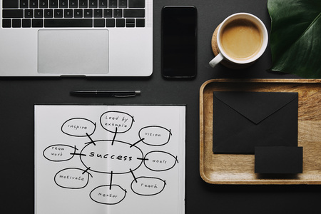 Open notebook with "success" icons by stationery and laptop on black backgroundの写真素材