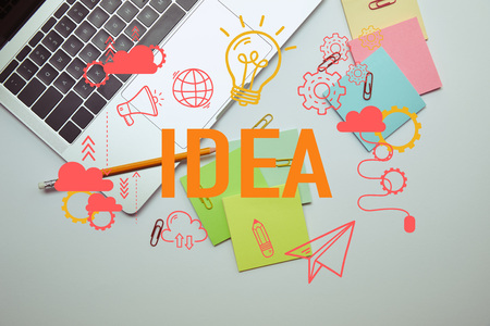 top view of laptop, paper stickers, pencil and paper clips on white tabletop with "idea" lettering and iconsの写真素材