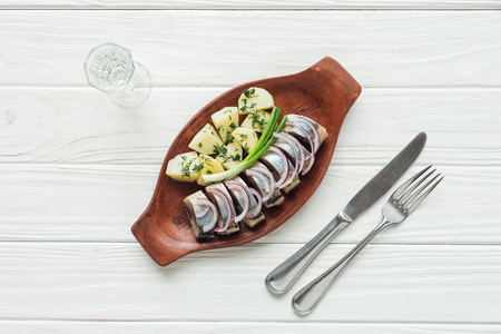 top view of marinated herring, potatoes and onions in earthenware plate with glass of vodka and...