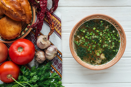 traditional fish soup with green onion, embroidered towel, mini pies and ingredients on white wooden backgroundの写真素材