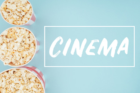 top view of buckets with popcorn in vertical row and "cinema" lettering isolated on blueの写真素材