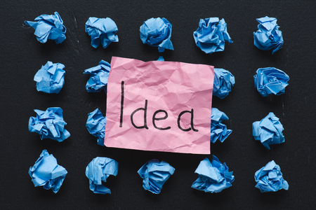 top view of 'idea' word written on sticky note with blue crumpled paper balls on black background, ideas conceptの写真素材