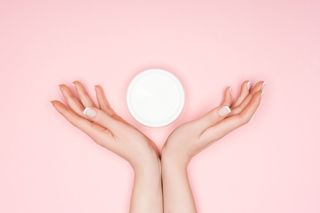 cropped view of female hands with body cream isolated on pinkの写真素材