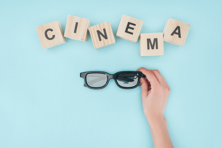 top view of wooden cubes with "cinema" lettering and hand holding 3d glasses isolated on blueの写真素材