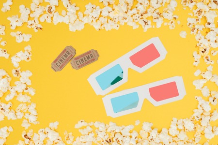 cinema tickets and 3d glasses in frame made of tasty popcorn isolated on yellowの写真素材