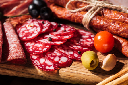 close up view of wooden cutting boards with delicious smoked sausages, vegetables and sliced salamiの写真素材
