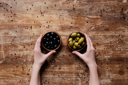 female hands holding two bowls with black and green olives on wooden tableの写真素材