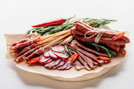 round cutting board with chili, herbs and delicious salami, prosciutto and smoked sausages  on brown wrapping paperの写真素材