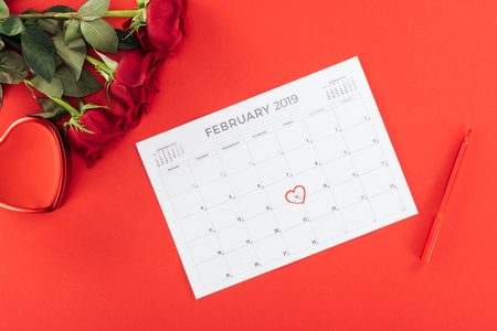 top view of roses and calendar with 14th february date marked with heart isolated on red, st valentines day conceptの写真素材