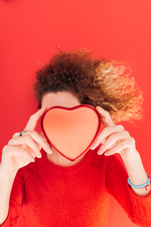 top view of girl holding heart symbol in front of face isolated on red, st valentines day conceptの写真素材