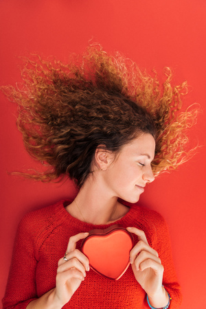 top view of beautiful girl holding heart symbol isolated on red, st valentines day conceptの写真素材