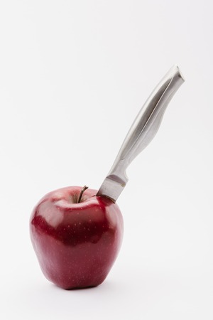 carving knife in whole red delicious apple isolated on whiteの写真素材