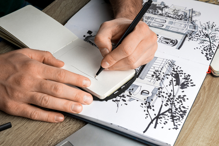 selective focus of mans hands drawing in notebook on wooden table next to albumの写真素材