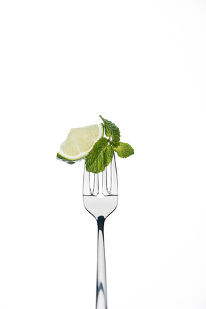 slice of lime and mint leaves on fork isolated on whiteの写真素材