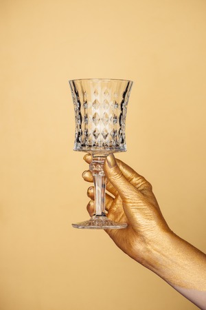 cropped view of female painted hand with vintage glass isolated on goldの写真素材