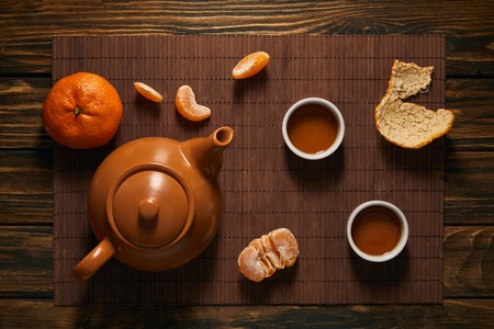 top view of teapot, cups of tea and tangerines on bamboo matの写真素材