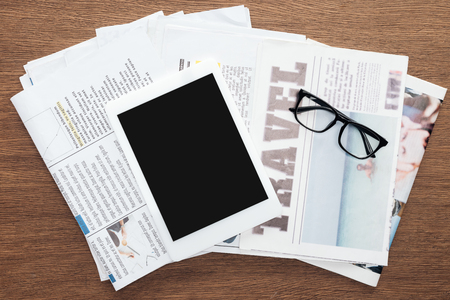 top view of tablet with blank screen, glasses and newspapers on wooden tabletopの写真素材