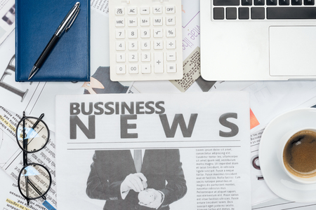 elevated view of eyeglasses, pen, calculator and notebook and laptop on newspapersの写真素材
