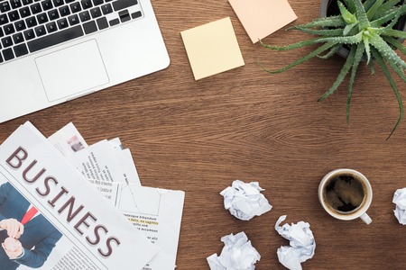 top view of laptop, business newspapers, potted plant and cup of coffee on wooden tabletopの写真素材