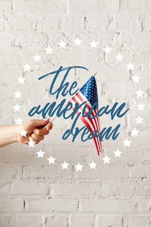 cropped image of man holding american flagpole against white brick wall with the american dream illustrationの写真素材