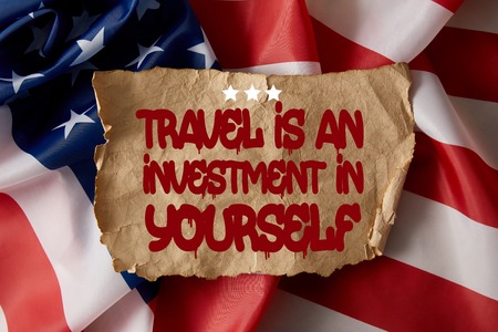 vintage crumpled paper with travel is an investment in yourself quote on american flagの写真素材