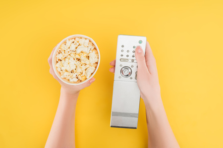 top view of hands holding popcorn bucket and remote controller isolated on yellowの写真素材