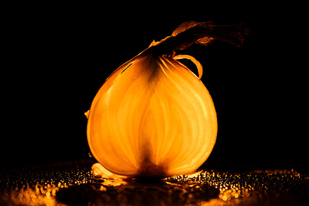 slice of raw onion with water drops and orange back light on black backgroundの写真素材