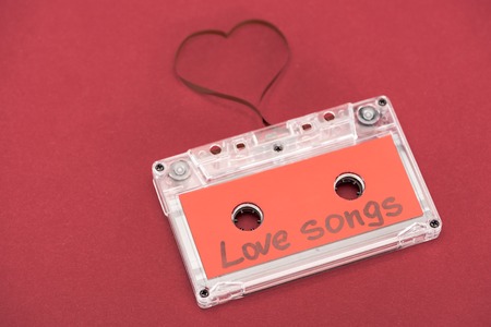 close up view of audio cassette with lettering love songs and heart symbol made of tape isolated on red, st valentine day conceptの写真素材
