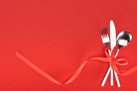 view from above of fork, knife and spoon wrapped by red festive ribbon isolated on red, st valentine day conceptの写真素材