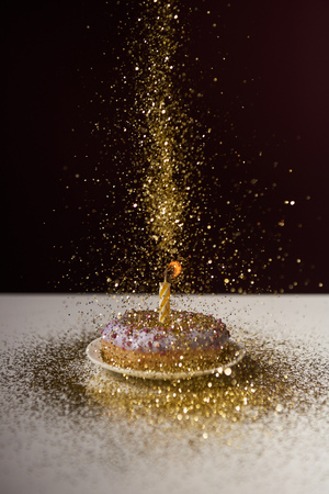 burning candle in middle of doughnut with falling golden sparkles isolated on blackの写真素材